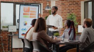company employee presenting business strategy with charts monitor planning project workmates analyzing financial statistics display working together company development 2 1 Smart4Ethiopia